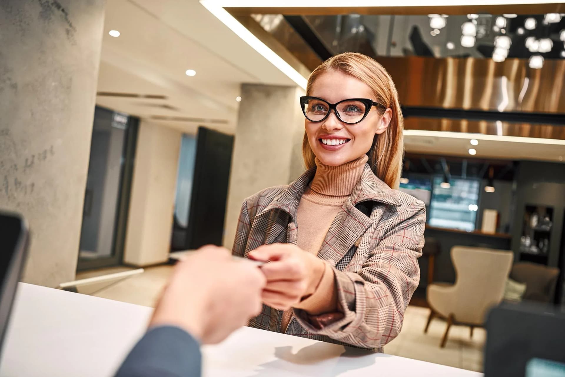 A smiling guest and a front desk agent pass a card across a hotel reception desk