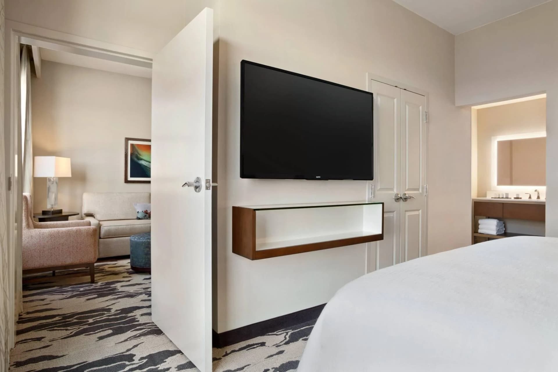 Suite at Embassy Suites McAllen with a wall TV beside the bed and a separate living room through an open door