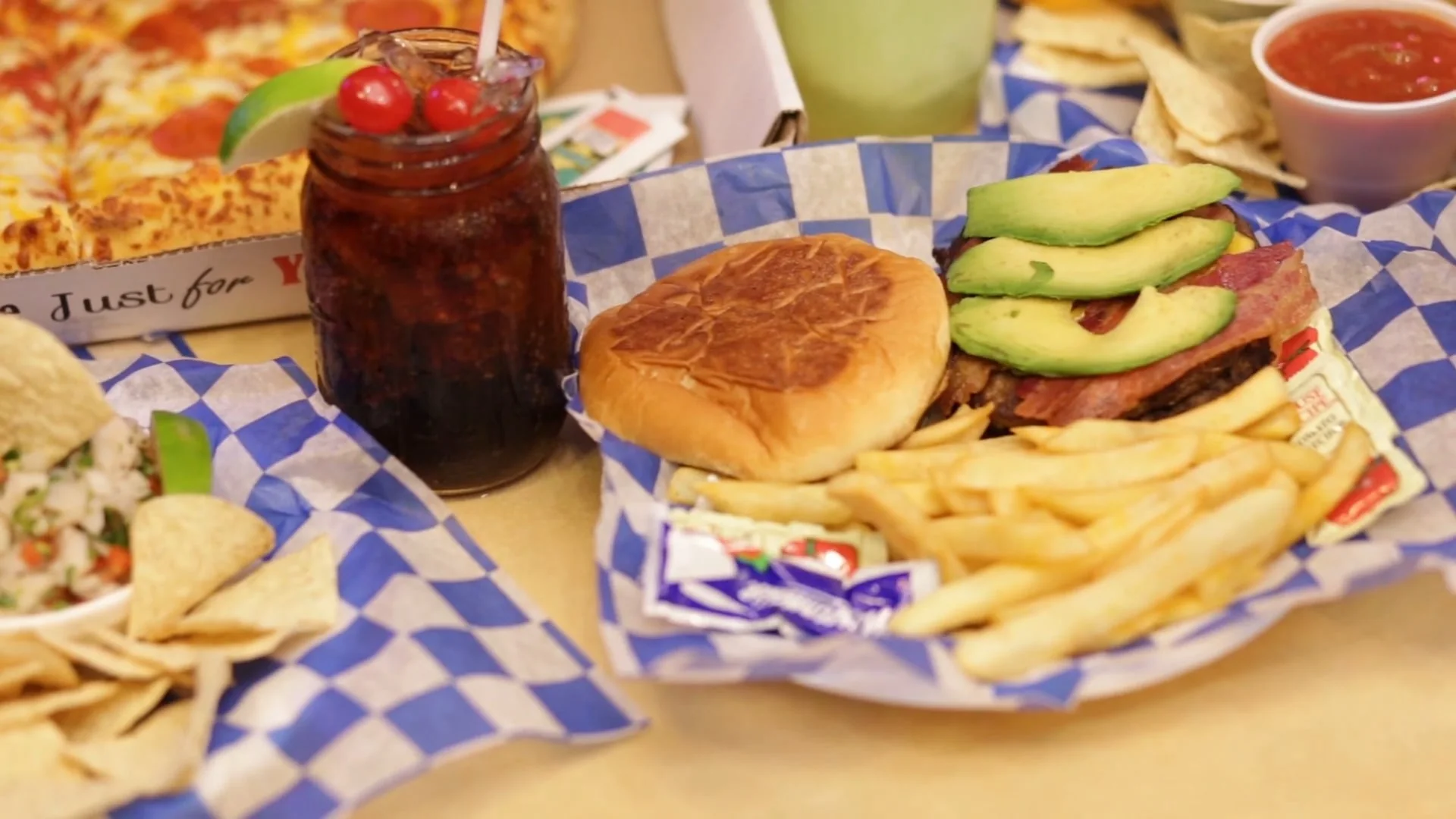 Bacon avocado burger with fries, tortilla chips and a cherry-topped drink in a mason jar